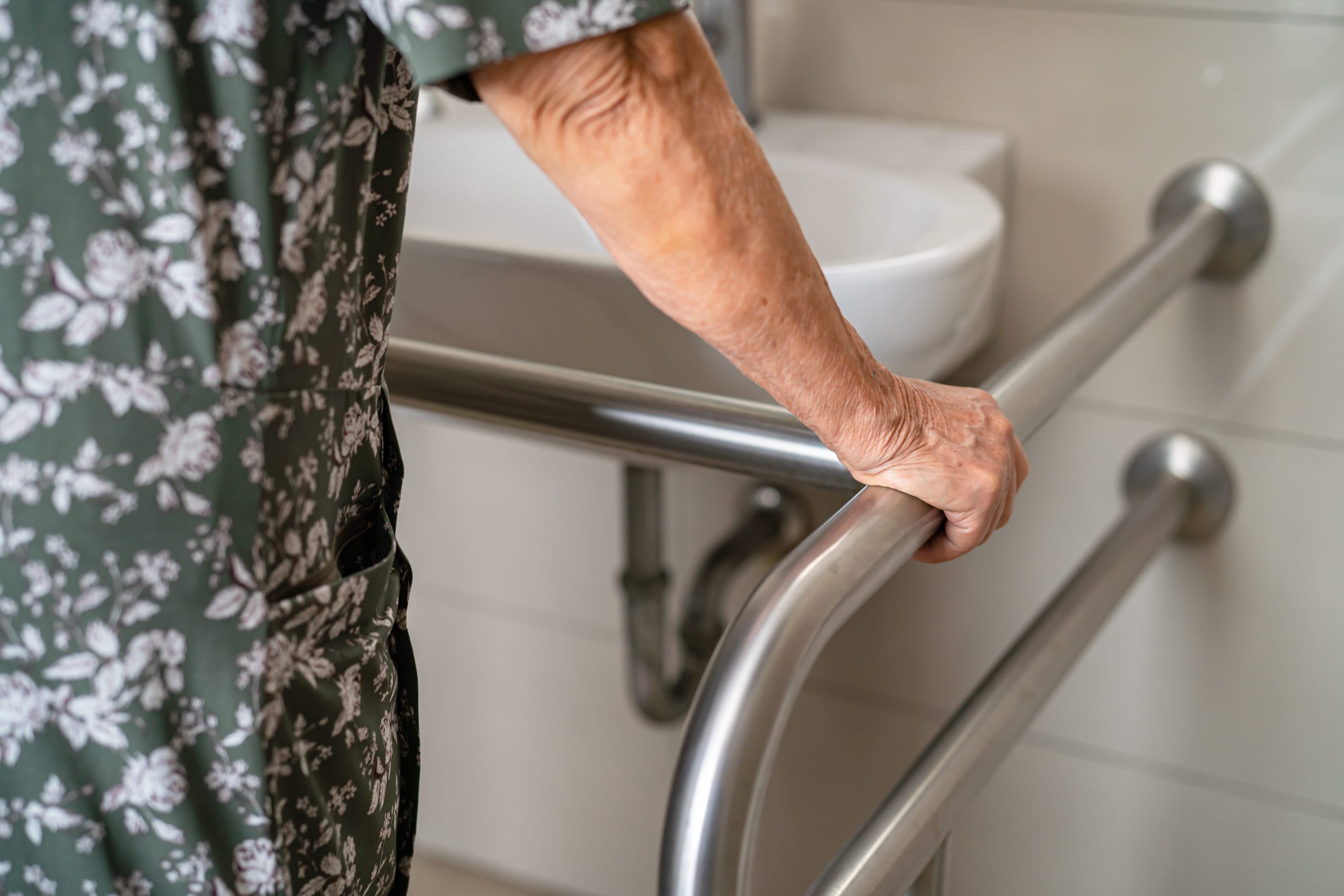 femme âgée s'appuyant sur une barre de soutien dans une salle de bain moderne