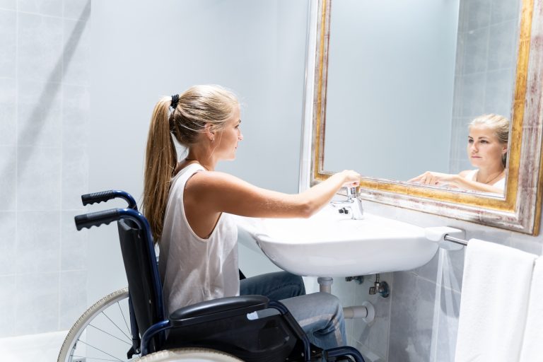 Une jeune fille en fauteuil roulant active le robinet d'eau dans une salle de bain accessible.